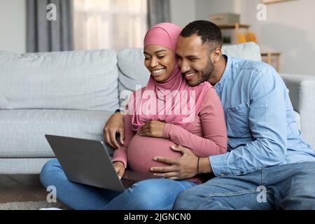 Amorevole sposi islamici neri che aspettano il bambino usando il portatile a casa Foto Stock