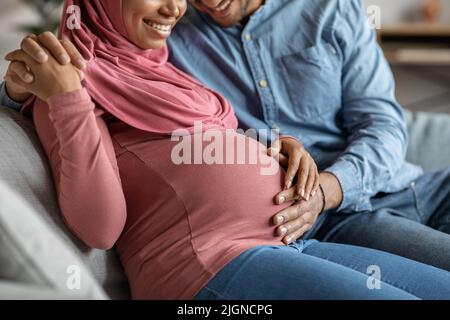 Buona gravidanza. Amorevole marito che tocca teneramente Belly della moglie musulmana incinta Foto Stock