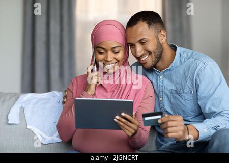 Concetto di e-commerce. Coniugi musulmani incinta che utilizzano il tablet digitale e la carta di credito Foto Stock