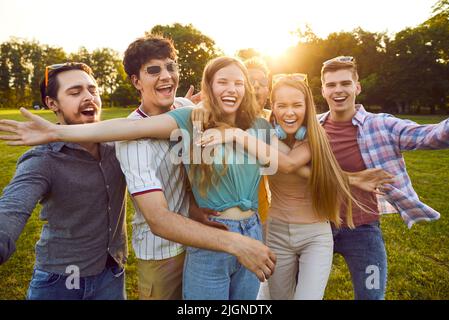 Gruppo di giovani amici felici e spensierati che stanno ridendo nel parco estivo con le braccia aperte alla fotocamera. Foto Stock