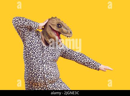 Divertente eccentrico uomo grasso vestito in stampa leopardo pigiama ballare con maschera dinosauro sulla sua testa. Foto Stock