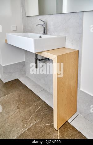 Moderno lavandino in ceramica con rubinetto installato su tavolo in legno in bagno. Ingegneria sanitaria con design elegante per interni bagno Foto Stock