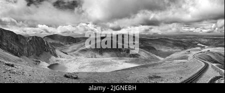 Panorama delle montagne di Snowdonia guardando dal Monte Snowdon, con un treno a vapore d'epoca che sale dalla città di Llanberis alla vetta. Nero Foto Stock