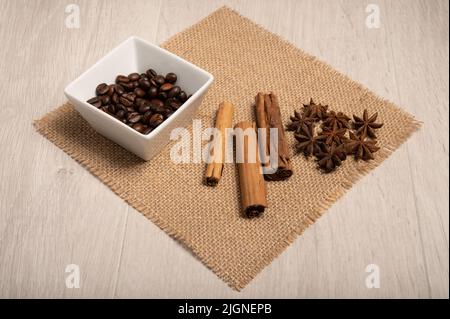 Cannella, anice stellato, chicchi di caffè da vicino su un panno hessian con uno sfondo di legno chiaro girato dall'alto Foto Stock