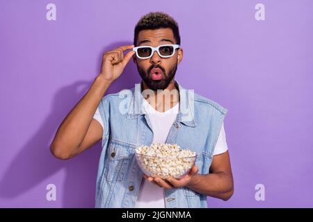 Foto di uomo impressionato eccitato indossano jeans gaistcoat occhiali scuri godendo pop mais isolato viola sfondo di colore Foto Stock