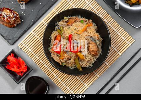 Spaghetti di vetro con verdure in una ciotola nera su sfondo grigio. Foto Stock