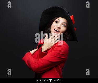 ritratto di una donna sorpresa in una giacca rossa e un cappello con un grande brim. foto sparare in studio su uno sfondo scuro Foto Stock