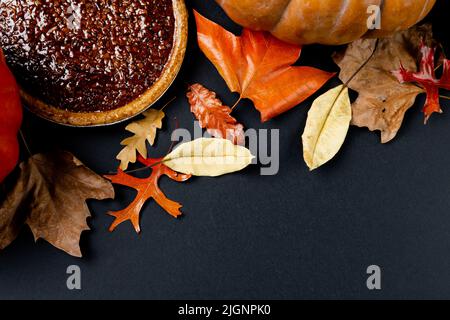 Composizione di zucche, foglie autunnali colorate e torta su sfondo nero Foto Stock