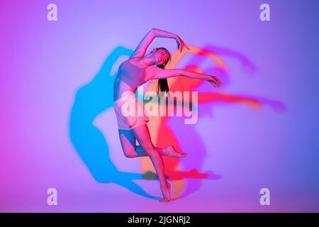 Ballare giovane ragazza in uniforme sportiva praticando isolato su sfondo gradiente studio in luce al neon. Contempla, danza, musica, sport, concetto giovanile. Foto Stock