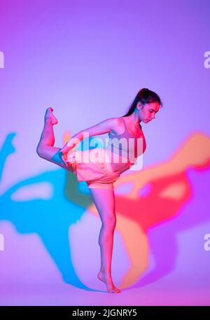 Ballare giovane ragazza in uniforme sportiva praticando isolato su sfondo gradiente studio in luce al neon. Contempla, danza, musica, sport, concetto giovanile. Foto Stock