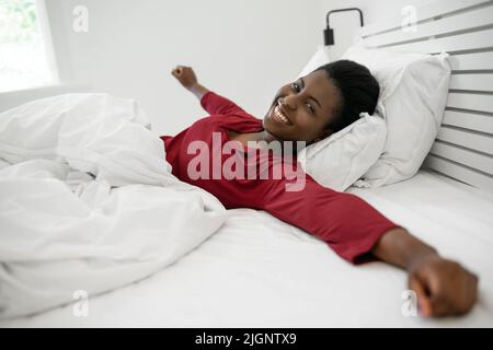 Bella donna africana svegliarsi al mattino, stretching e sorridendo, guardando in macchina fotografica Foto Stock