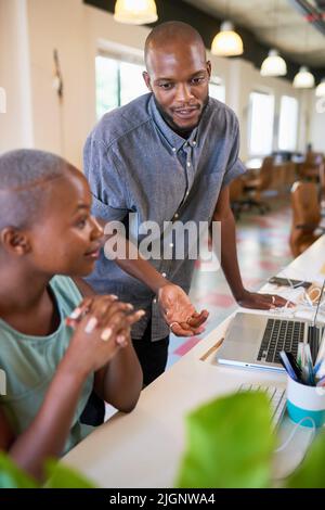 Due colleghi Creative Black discutono del lavoro nei loro computer in ufficio Foto Stock