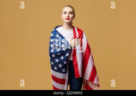 Bella bionda si pone con orgoglio con una bandiera americana. Foto sparare in studio su uno sfondo giallo. Foto Stock