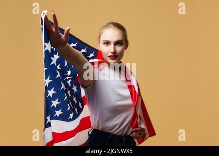 Bella bionda si pone con orgoglio con una bandiera americana. Foto sparare in studio su uno sfondo giallo. Foto Stock