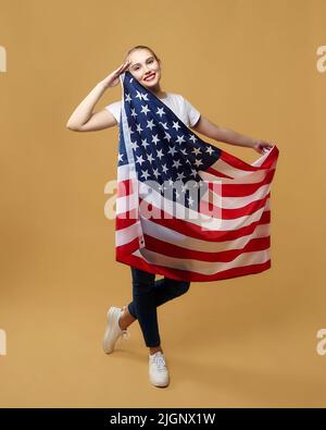 Bella bionda si pone con orgoglio con una bandiera americana. Foto sparare in studio su uno sfondo giallo. Foto Stock