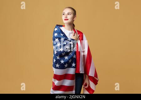 Bella bionda si pone con orgoglio con una bandiera americana. Foto sparare in studio su uno sfondo giallo. Foto Stock