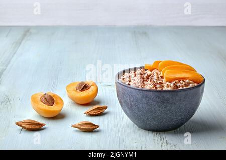 Colazione energetica. Fiocchi d'avena a grani interi con semi di lino e fette di albicocca su tavolo di legno blu dipinto. Vista frontale con spazio di copia Foto Stock