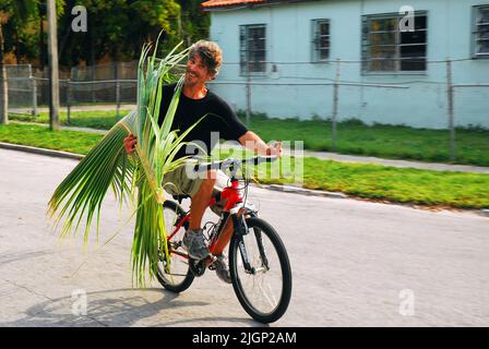 Un giovane uomo porta un fronte da una palma mentre guida la sua bicicletta per portare a una celebrazione del Mercoledì delle Ceneri in una chiesa di Miami Foto Stock