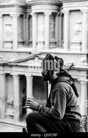 Una guida beduina locale seduta giù bere caffè oveleooking l'esterno del Tesoro 'al-Khazneh', da Un punto di vista alto, Petra, Giordania. Foto Stock