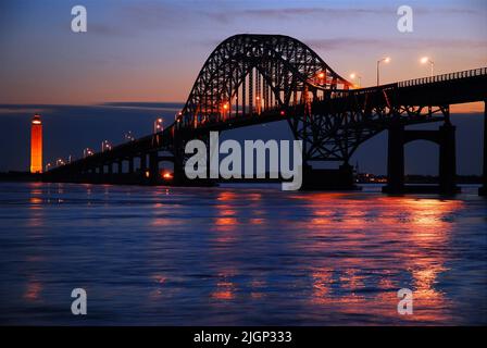 Le luci del ponte ad arco in acciaio Robert Moses Causeway si riflettono nelle acque della baia e conduce ad un faro su Long Island Foto Stock