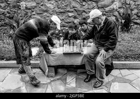 Due uomini che giocano a Scacchi guardati da bambini locali, Pisac, la Valle Sacra, Provincia di Calca, Perù. Foto Stock