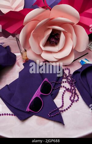 Omaggi di festa sul tavolo al matrimonio con grande fiore di carta, occhiali da sole viola e tovaglioli viola. Foto Stock