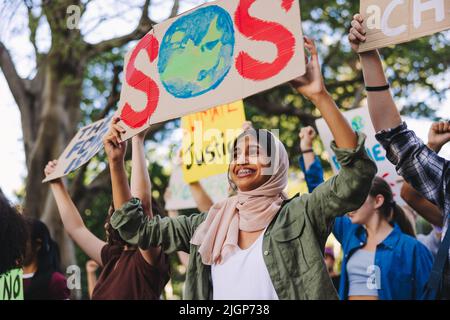 Giovani diversi che si alzano per la terra. Gruppo di attivisti giovanili multiculturali che portano poster mentre si battono contro il cambiamento climatico. Felice y Foto Stock