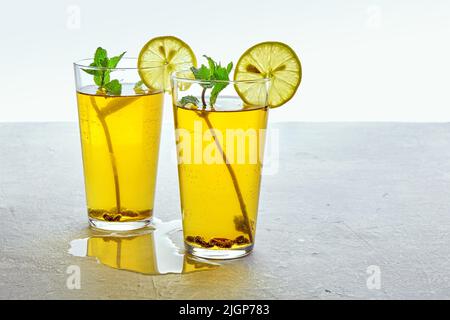 Due tazze di vetro di tè Kombucha fermentato fatto in casa sono decorate con menta e limone su un tavolo di cemento grigio chiaro. Bevanda a basso contenuto di alcol gassato su un Foto Stock