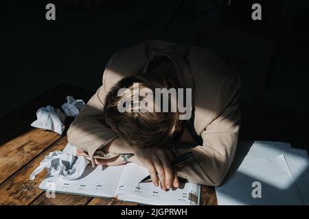 Burnout, problemi emotivi, concetto di depressione. Triste stanca depressa donna sdraiata sul tavolo tra carte Foto Stock