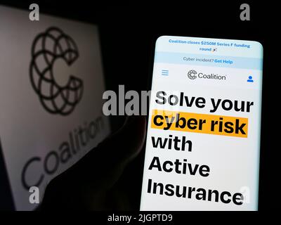 Persona che tiene smartphone con la pagina web della compagnia di assicurazione informatica statunitense Coalition Inc. Sullo schermo con il logo. Concentrarsi sul centro del display del telefono. Foto Stock