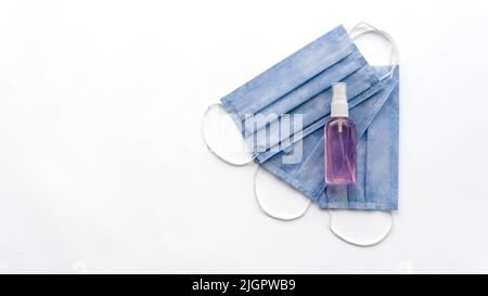 Primo piano di COVID-19 e degli strumenti di protezione contro i virus. Tre maschere mediche blu e gel igienizzante viola. Isolato su sfondo bianco. Tema coronavirus. Foto Stock