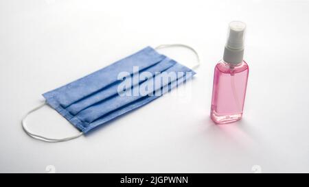 Foto ravvicinata della protezione da coronavirus. Maschera medica blu e gel igienizzante rosa isolato su sfondo bianco Foto Stock