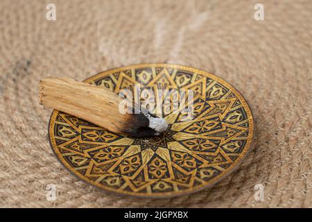 Palo santo bastone di legno che brucia e fuma su un vassoio d'oro fuoco selettivo primo piano Foto Stock