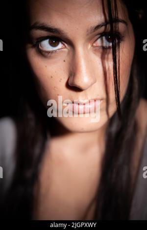 Ansia scura. Uno sguardo preoccupato sul volto di una bella giovane razza mista Anglo-indiana modello femminile in un luogo buio. Da una serie con lo stesso modello. Foto Stock
