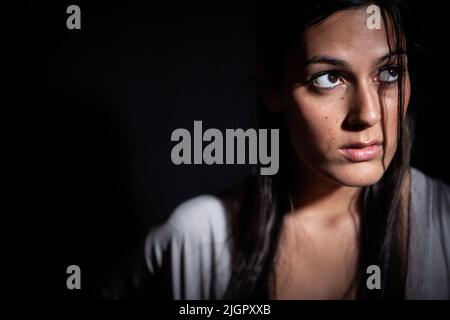 Paura oscura. Uno sguardo preoccupato sul volto di una bella giovane razza mista anglo-indiana modello femminile in un luogo buio. Da una serie con lo stesso modello. Foto Stock