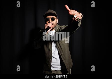 hip hop indiano in occhiali da sole cantando in microfono su nero Foto Stock