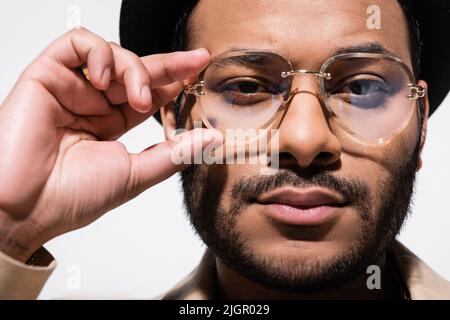 primo piano del performer indiano di hip hop in fedora hat regolazione occhiali isolati su grigio Foto Stock