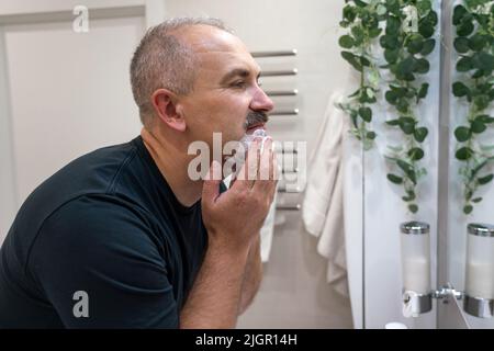 Uomo che rasa con il rasoio utilizzando schiuma in bagno al mattino Foto Stock