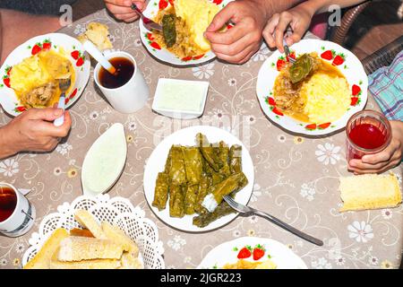 La famiglia al tavolo rotondo prende il cibo, vista dall'alto. Pranzo: dolma con salsa, purè di patate e cavolo. Foto Stock