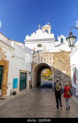 Coppia Turistica in pensione a piedi per l'Arco da Vila Faro Portogallo uno dei cancelli originali nella Città Vecchia di Faro l'Algarve Portogallo, due Storks Foto Stock