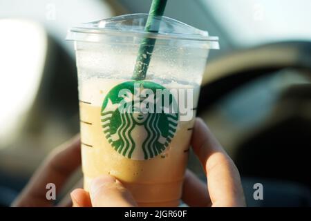 Una persona che tiene una tazza di caffè Starbucks in auto. Foto Stock