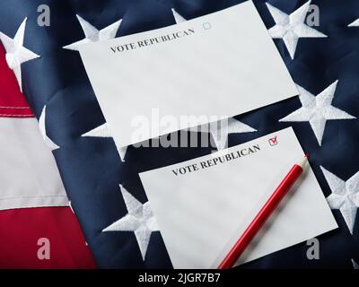 Fogli di carta con le iscrizioni votano repubblicano e votano democratico, una matita sullo sfondo della bandiera americana di stato. Primo piano. Camma elettorale Foto Stock