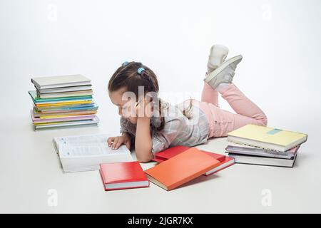 piccola ragazza affascinante con pigtail intrecciato in studio su uno sfondo bianco, un sacco di libri sono sparsi intorno a lei. Foto Stock