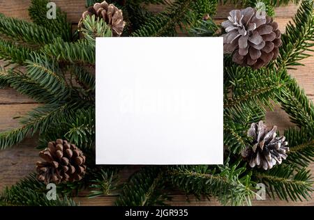 Modello mockup di carte 5x5 Natale su rametti di abete naturale su sfondo di legno. Elemento di design per le congratulazioni di Natale e Capodanno, rsvp, grazie Yo Foto Stock