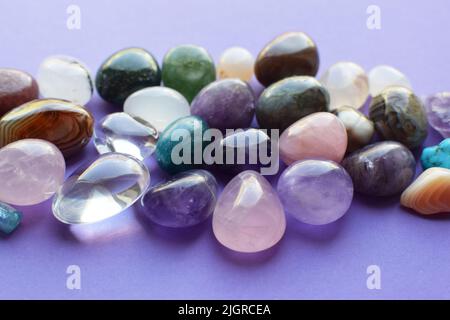 Gemme tumbled di vari colori. Ametista, quarzo rosa, agato, apatite, aventurina, olivina, turchese, acquamarina, cristallo di roccia su sfondo viola. Foto Stock