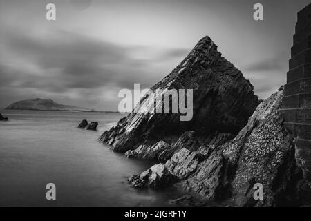 Una foto in scala di grigi di formazioni rocciose su una spiaggia Foto Stock