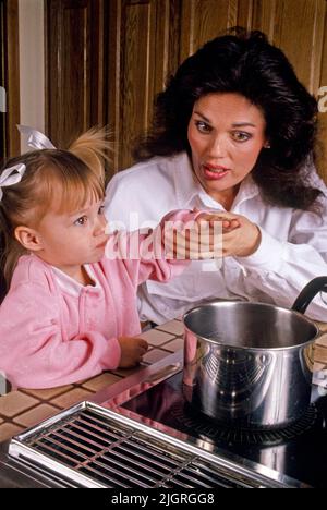 Tenendo la mano, una madre insegna la figlia del bambino circa i pericoli di calore alla stufa nella cucina della loro casa in Laguna Niguel, CA. Foto Stock