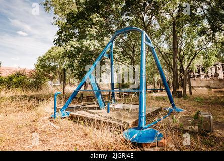 Una vista di un vecchio swing blu abbandonato in un parco giochi in una giornata di sole Foto Stock