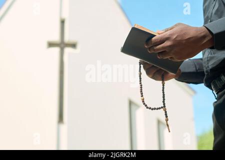 Mani di prete in abito nero che tengono perle di rosario e aprono il Vangelo mentre leggono i versi e li spiegano durante il sermone Foto Stock