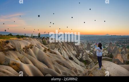 Smartphone in mani di donna fotografando un bellissimo paesaggio e palloncini in Cappadocia. Sunrise Time, concetto di viaggio sognante Foto Stock